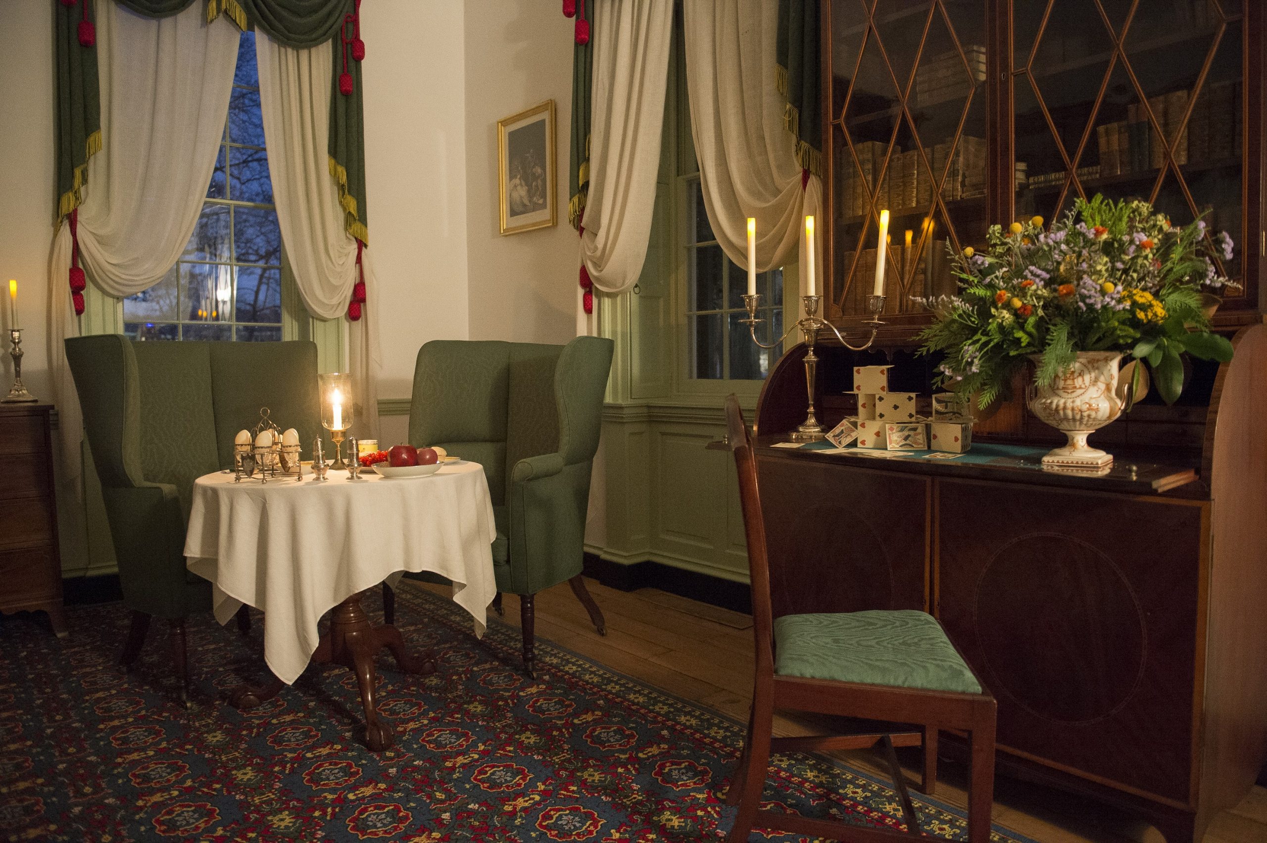 A secretary desk and two arm chairs and a small breakfast table in Homewood's Master Bed Chamber are decorated for the holidays and illuminated by candlelight