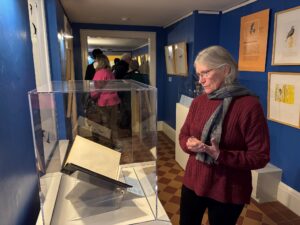 A woman stands in a gallery and looks at a rare book in an exhibit case.